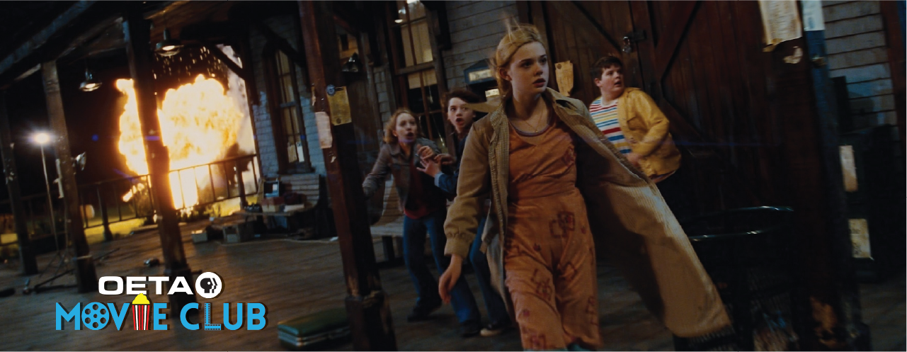 Scene from Super 8 showing five kids running from an explosion in a train station, with the OETA Movie Club logo in the corner