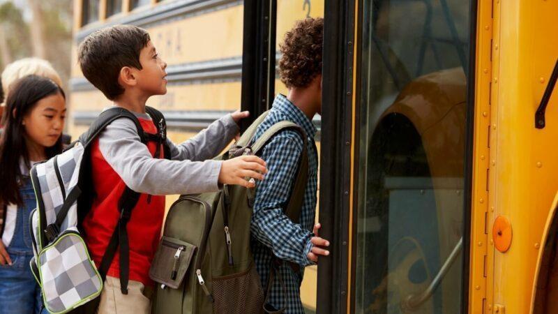 Three children with backpacks board a yellow school bus