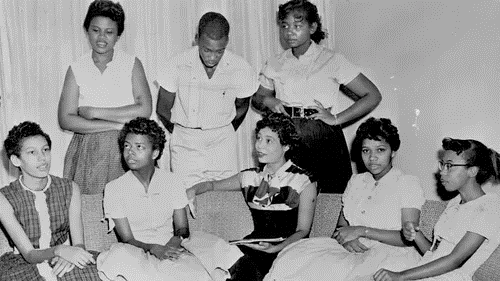 Black and white photo of eight young African American women seated and gathered around a sofa. 