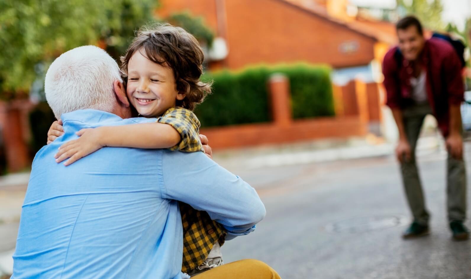 A young child hugs a grandparent while the father looks on smiling