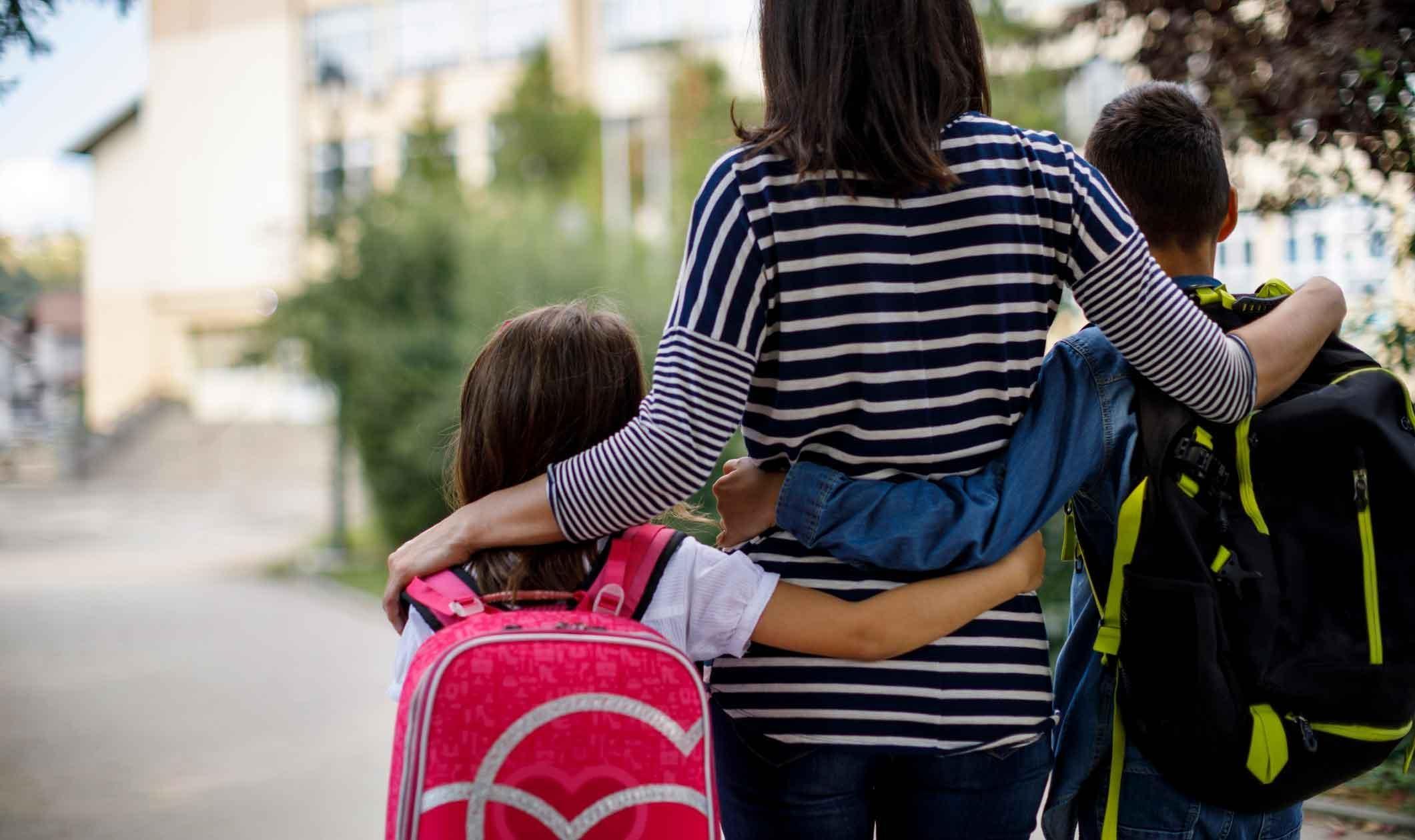 A mother stands with her hands on the shoulders of her children - one on each arm - as they prepare to go back to school. 