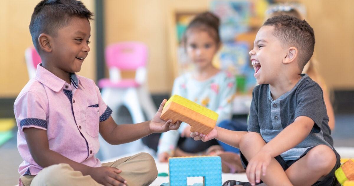 Two children smile and share blocks during playtime