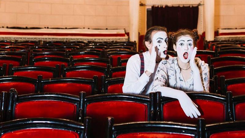 Two mimes look surprised while sitting in red theater seats
