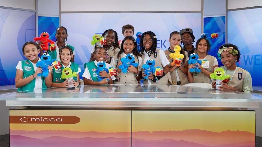 Girl Scouts posing with Sesame Street character plushies at the anchor desk on the Nevada Week TV studio set