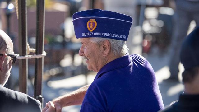 Man with white hair wears a purple t-shirt and a Purple Heart cap, looking off to the left