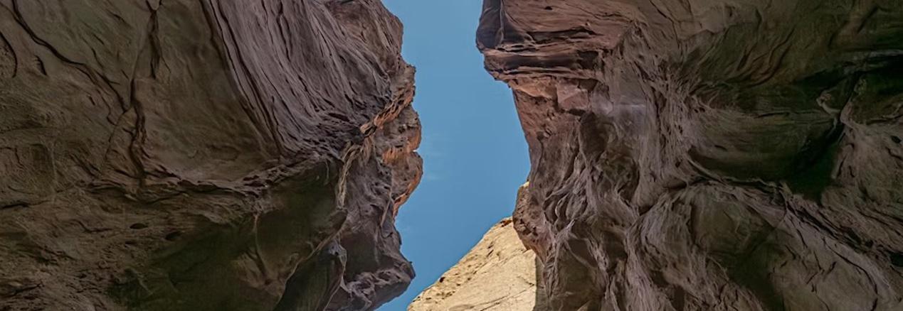 Looking up to a blue sky from the bottom of a canyon with the many textures of rock creating waves