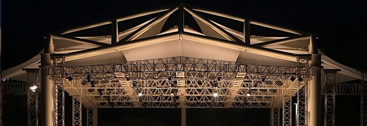 an outdoor amphitheater stage with lighting rigs lit up at night against a black sky
