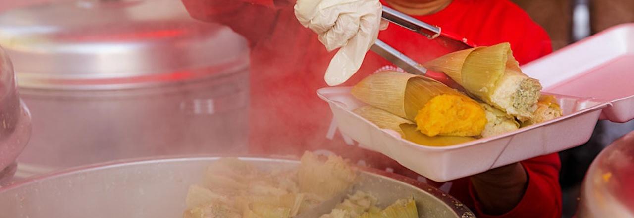 Tamales getting served in a styrofoam takeout container from a steaming pot
