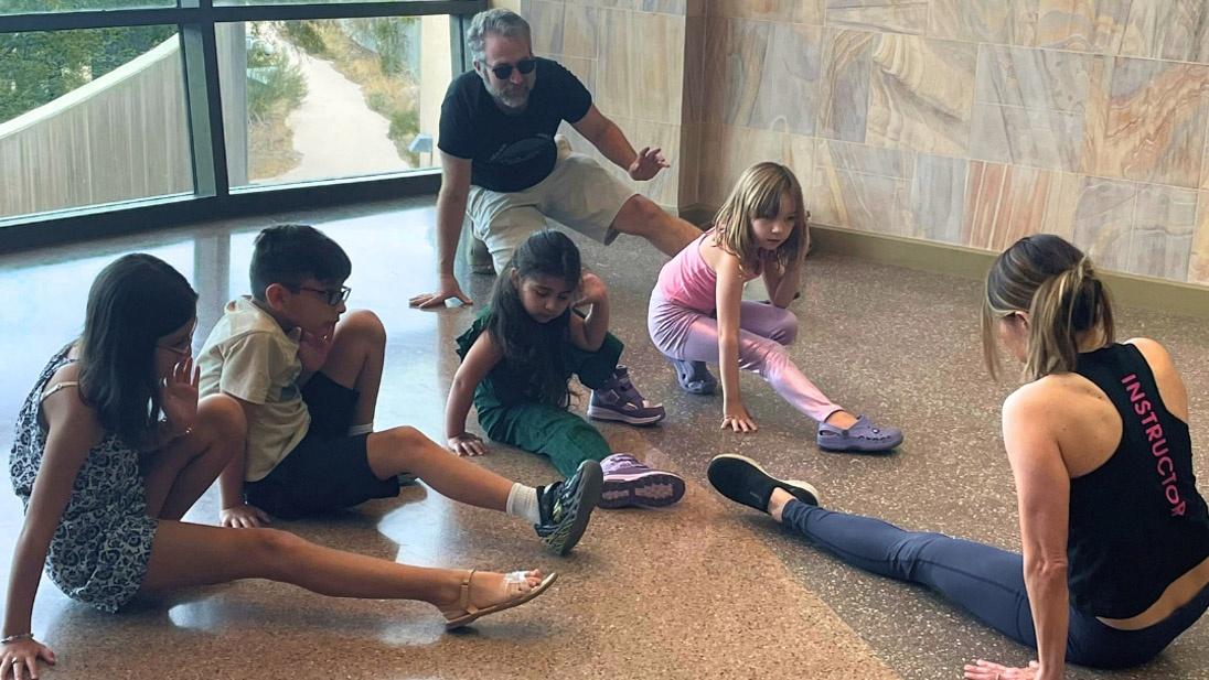 children practicing yoga poses on a museum floor with the help of an adult instructor