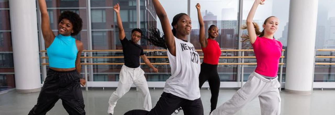 A group of dancers standing with their legs spread and their right arms up in the air
