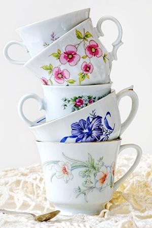 stack of five teacups with floral designs and a single spoon resting on the table next to the bottom cup