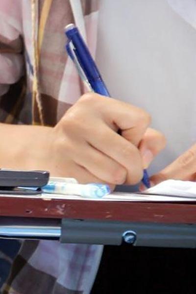 A hand holding a pen writes on a piece of paper on a desk