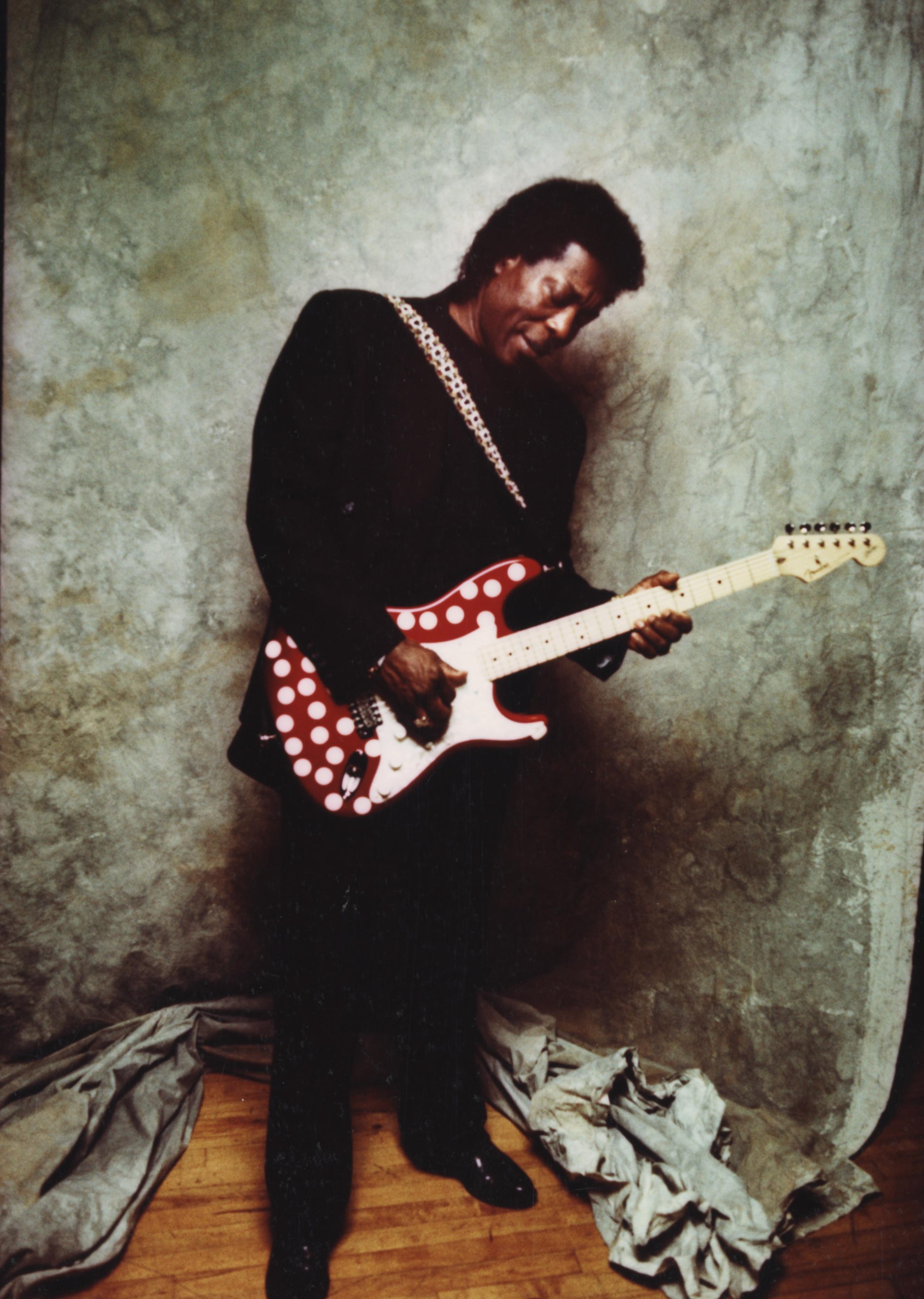 buddy guy against a backdrop playing a red guitar with white dots