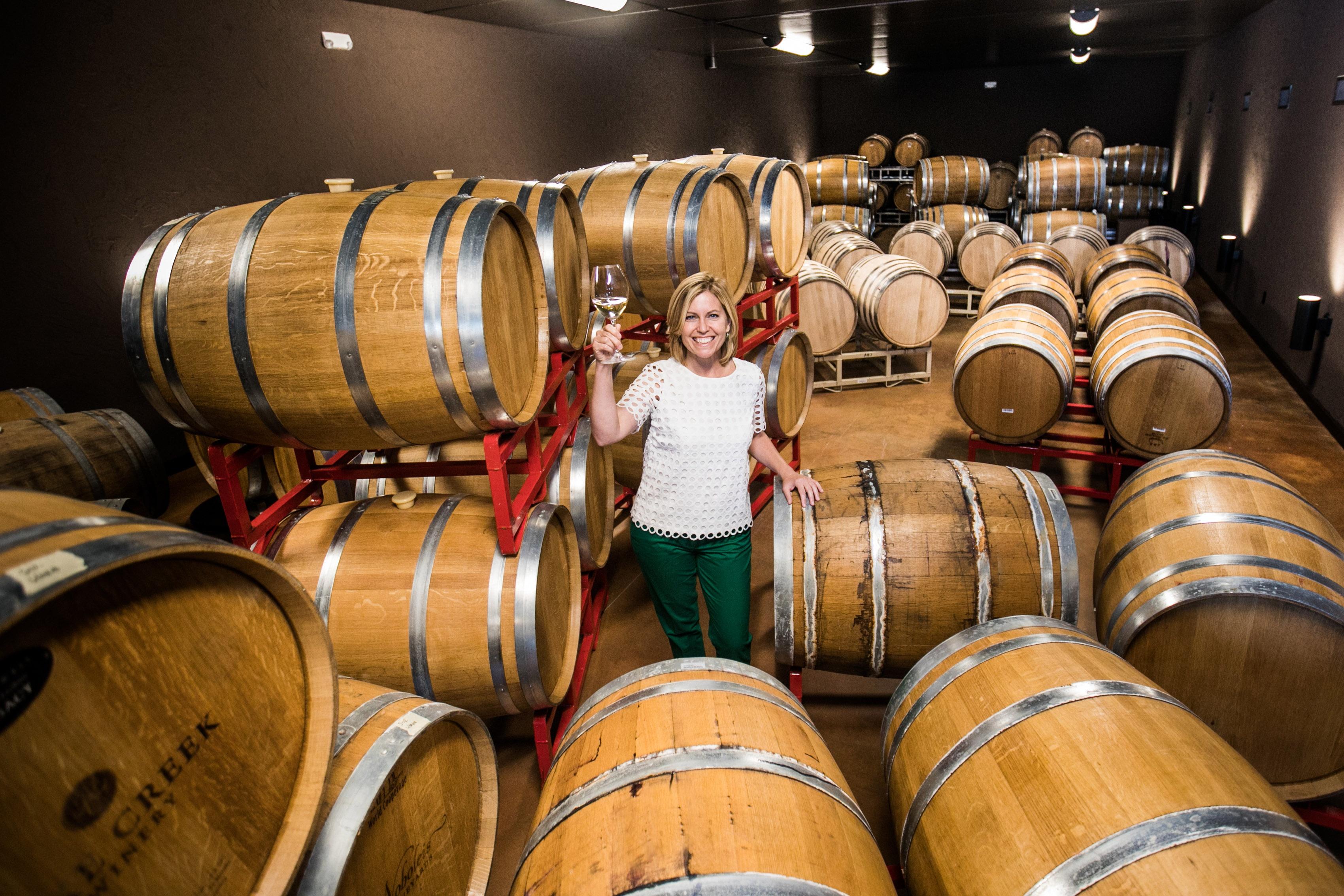 Host Cat Neville holds up a wine glass surrounded by wine barrels