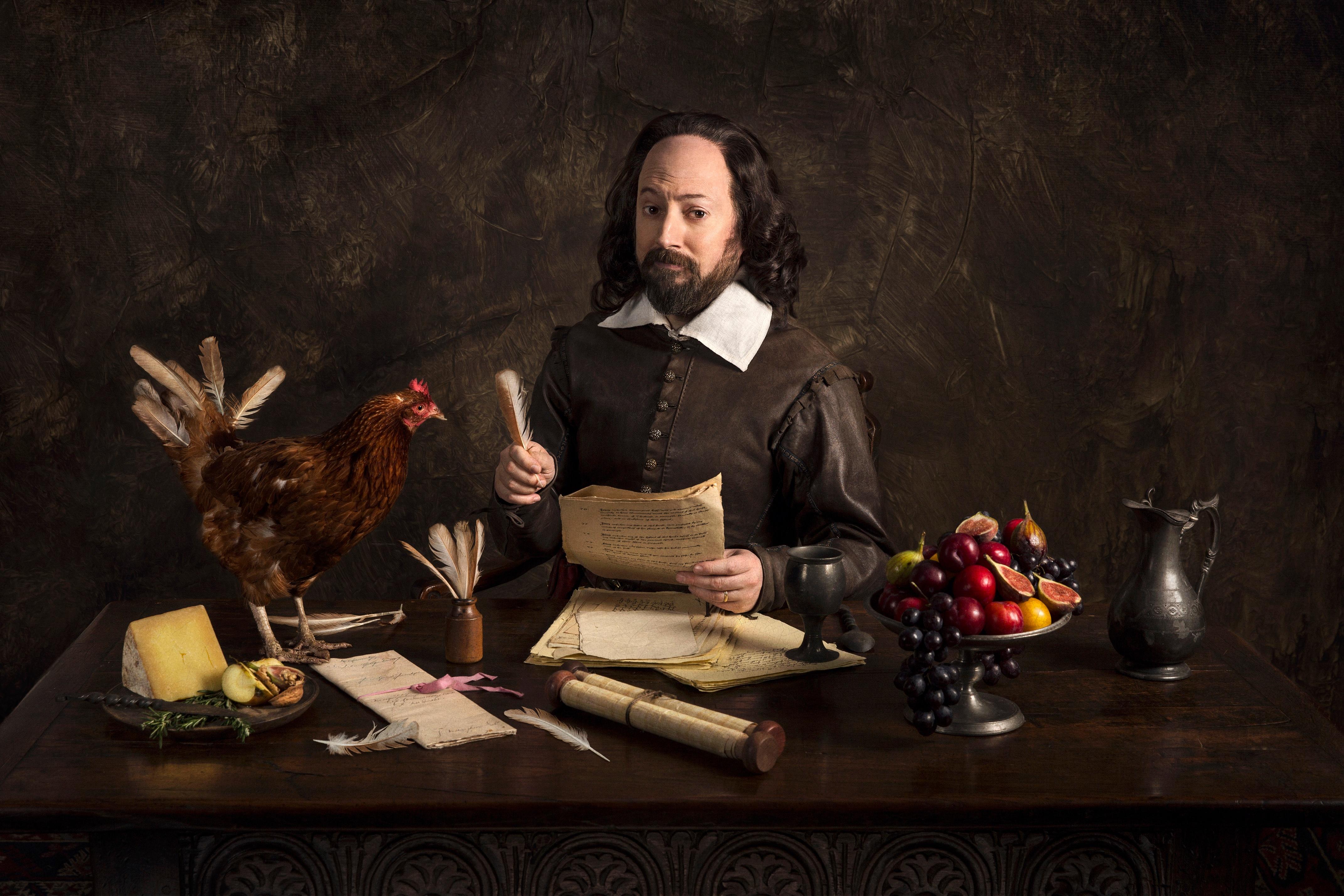William Shakespeare at a writing desk covered in items, including a chicken