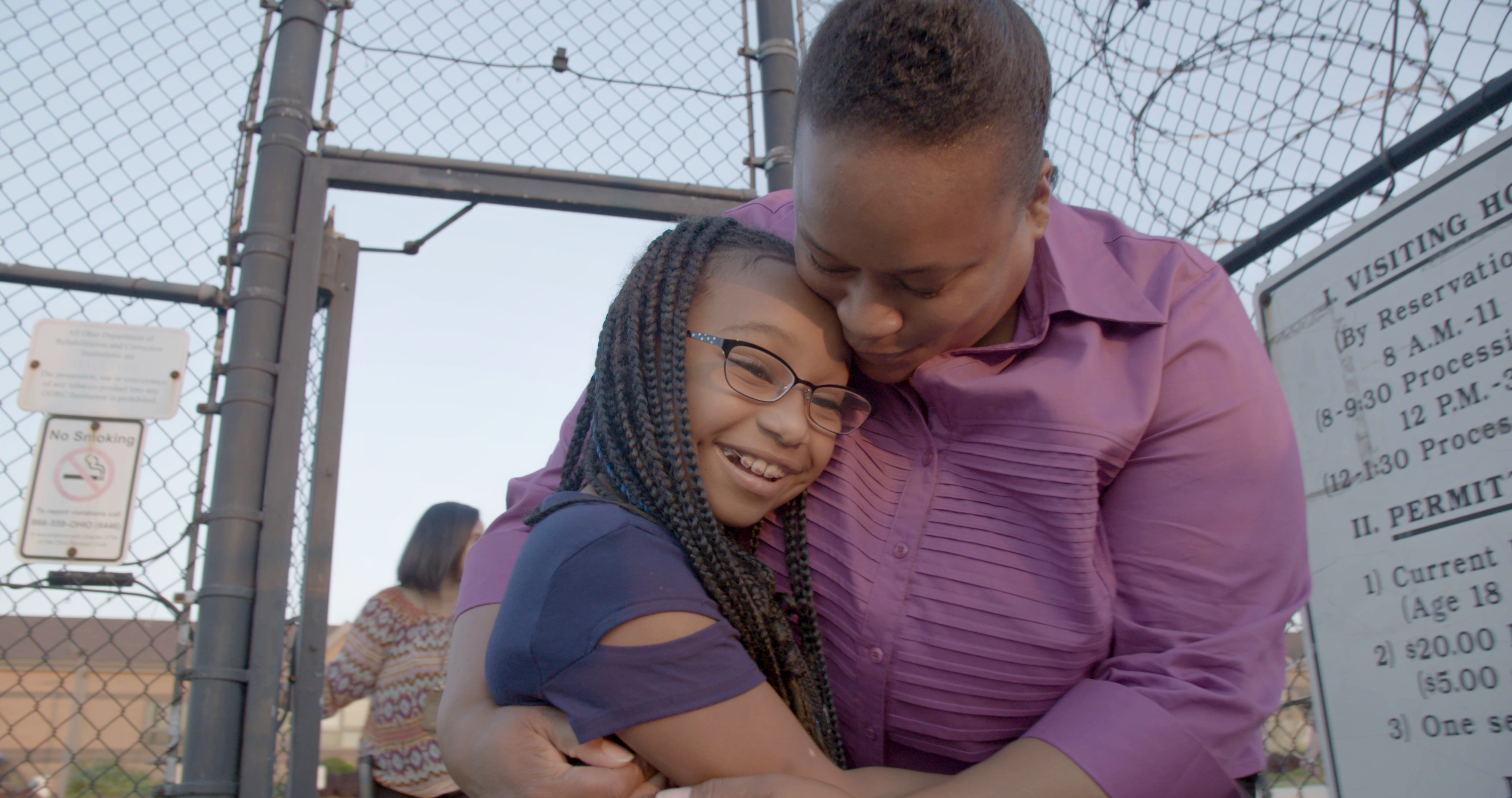 a black mother hugs her daughter outside the gates of a prison