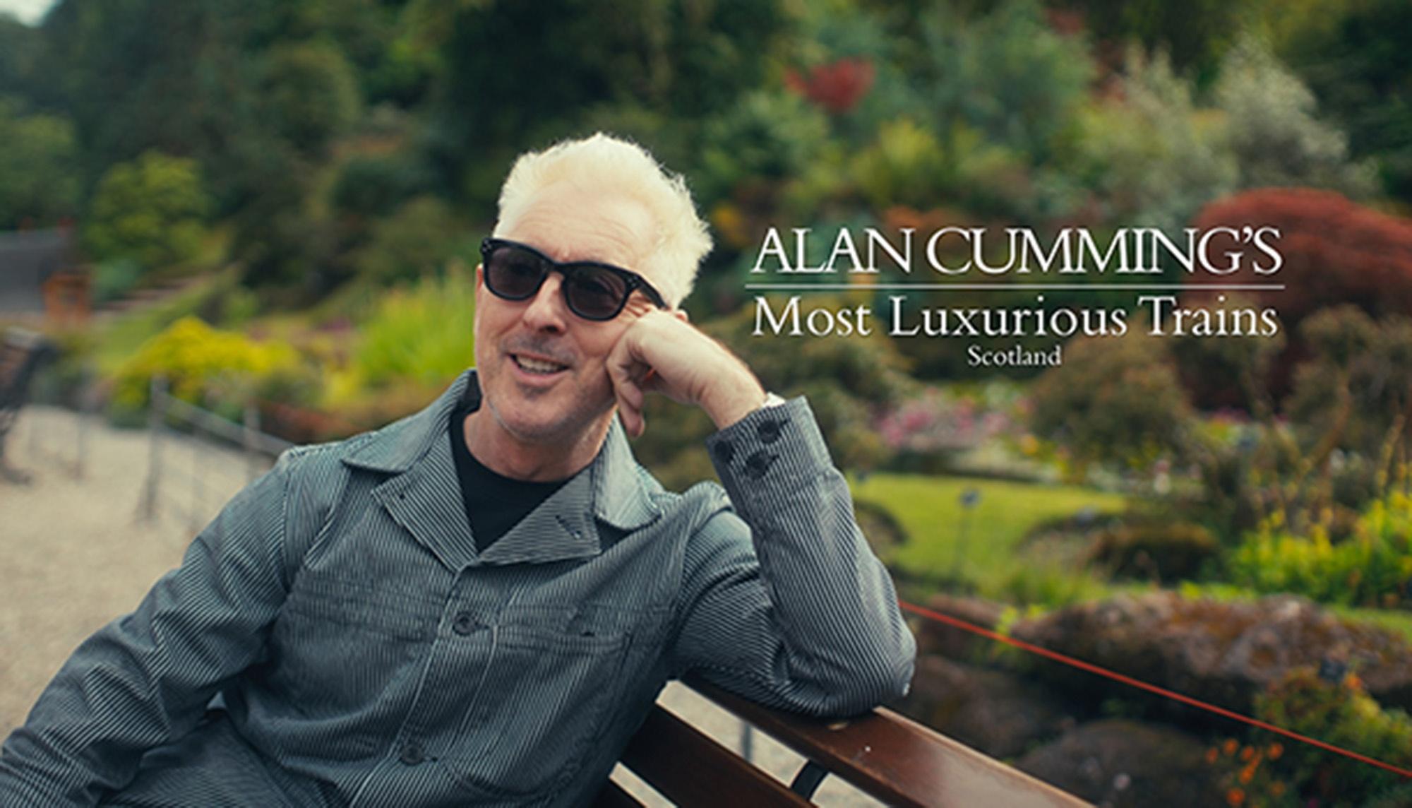 Alan Cumming sits on a bench looking at the camera with the title "Alan Cumming's Most Luxurious Trains Scotland".
