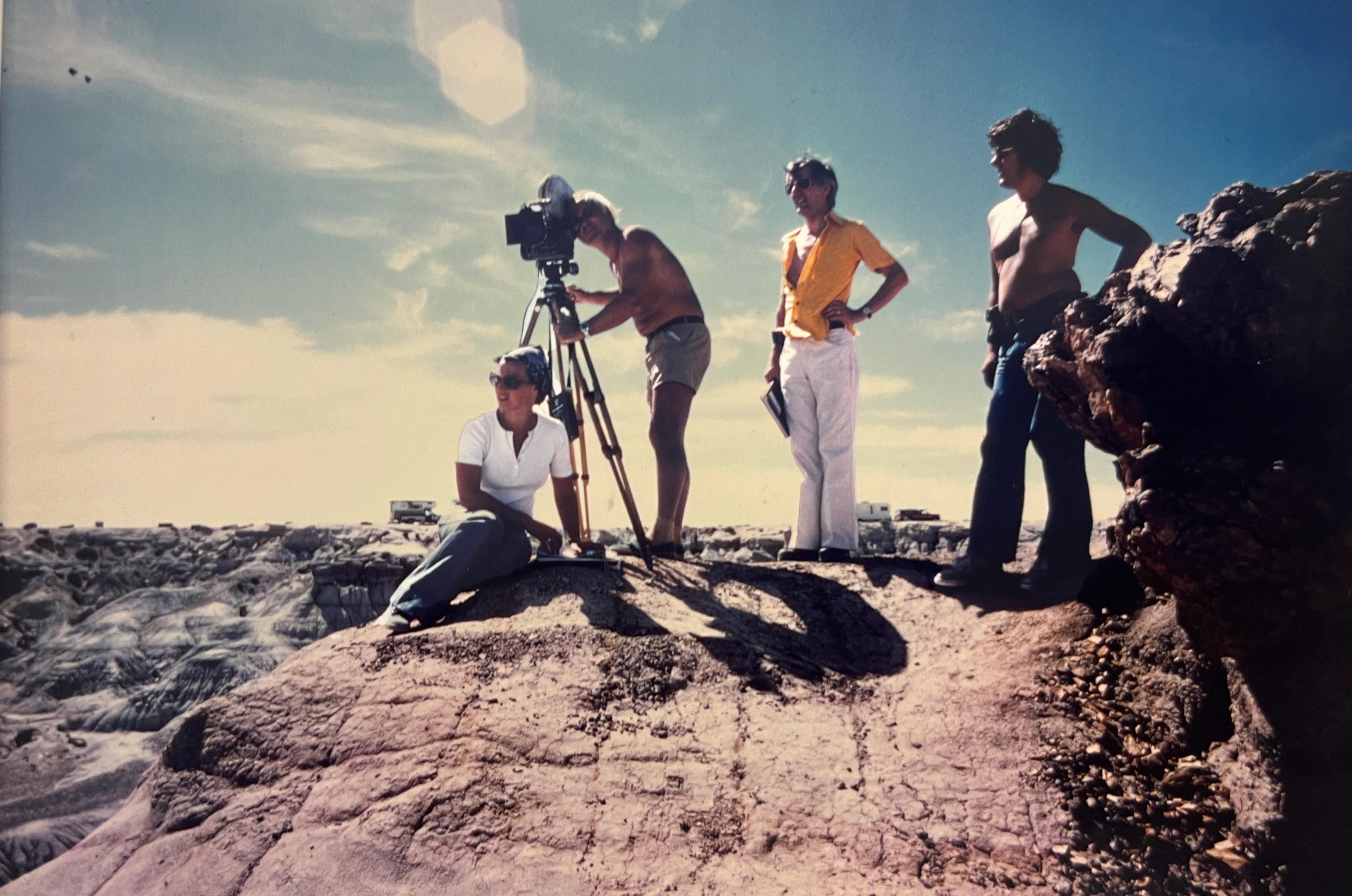 A cameraman, with 3 production crew members on a hill.