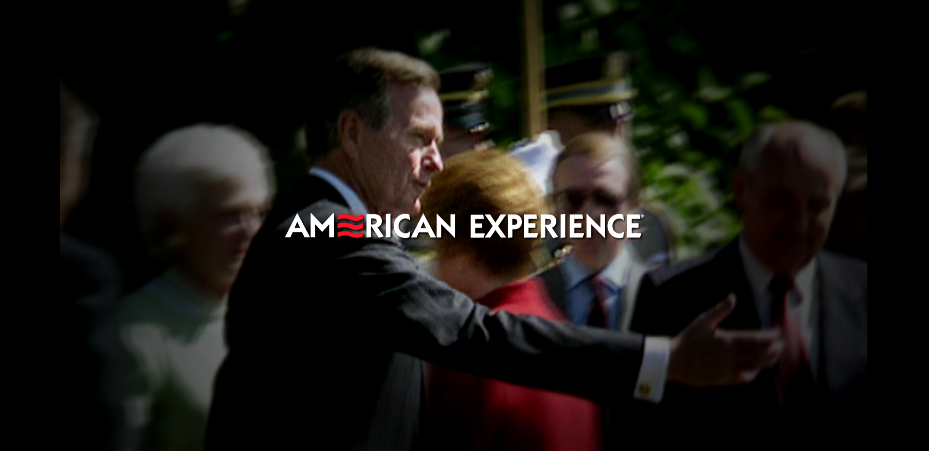 "American Express Graphic Text with the background being a blurred picture of George HW Bush formally dressed in a suit and extending his hand at an outdoor event with a lot of people.