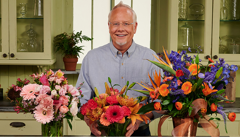 J. Schwanke stands smiling behind three bouquets of flowers.