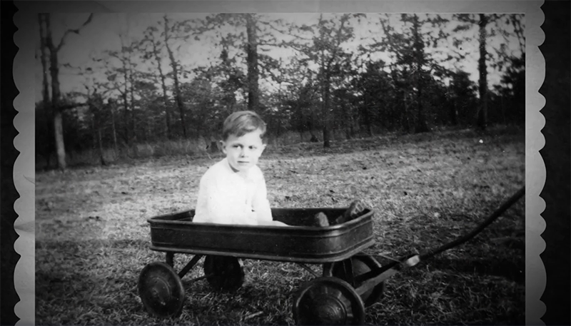 A black and white photo of the first person diagnosed with autism, Donald Gray Triplett, as a child, sitting in a wheelbarrow.