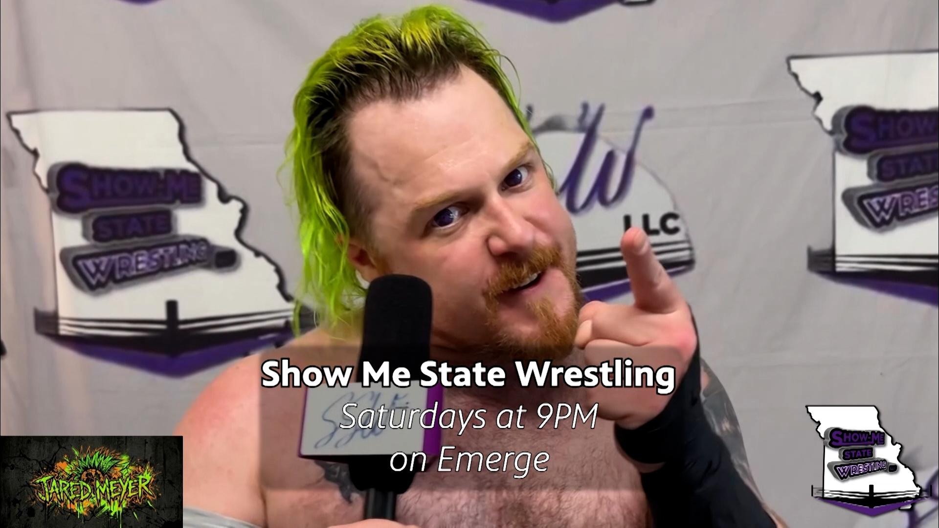 A wrestler holding a mic and pointing his finger in a dramatic fashion.