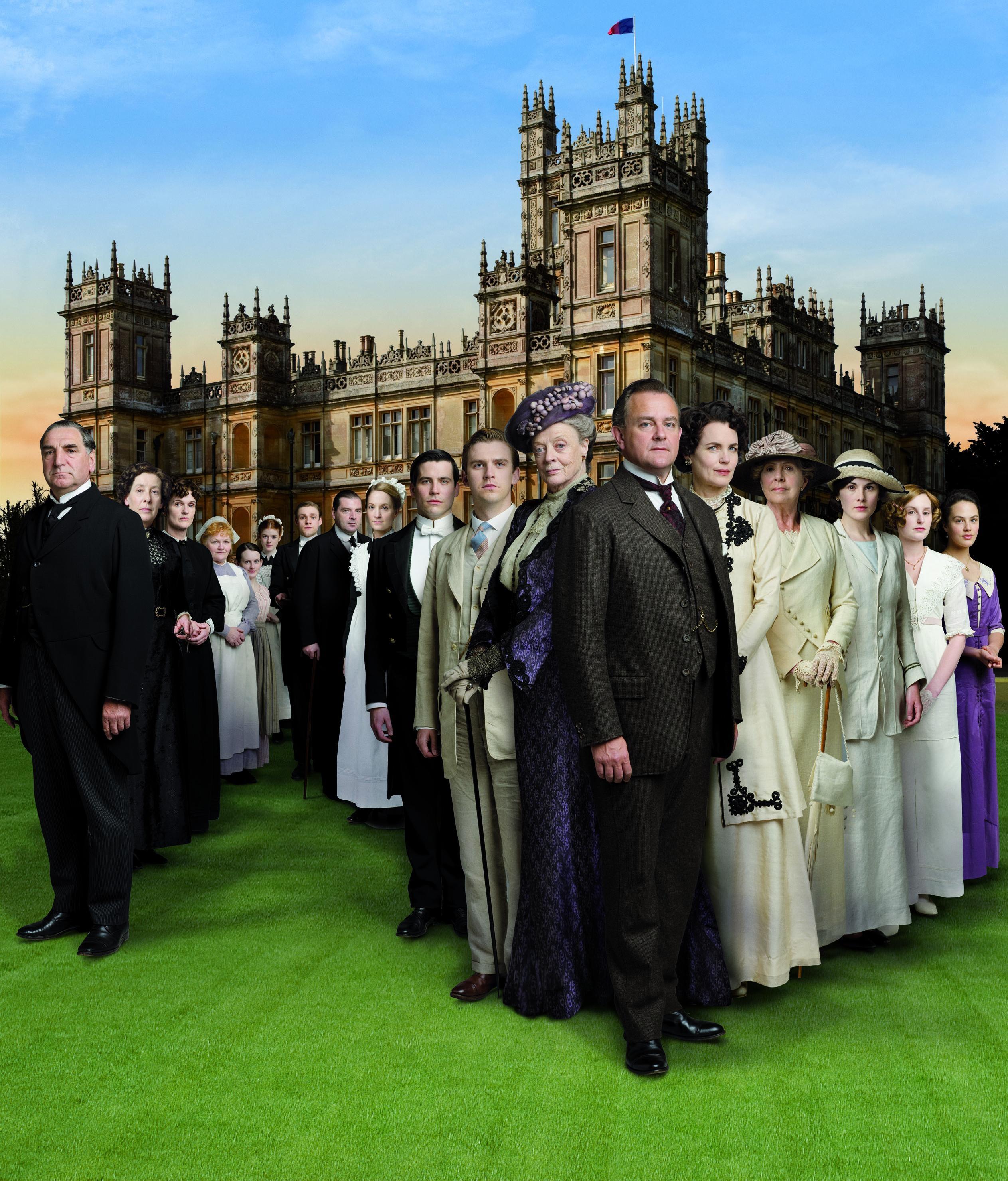 The Crawley family and their servants posing in elegant attire in front of the Downton Abbey.