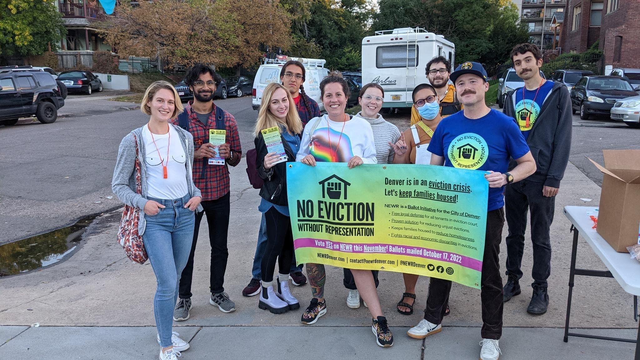 A group of NEWR canvassers smile holding a colorful No Eviction without Representation banner 