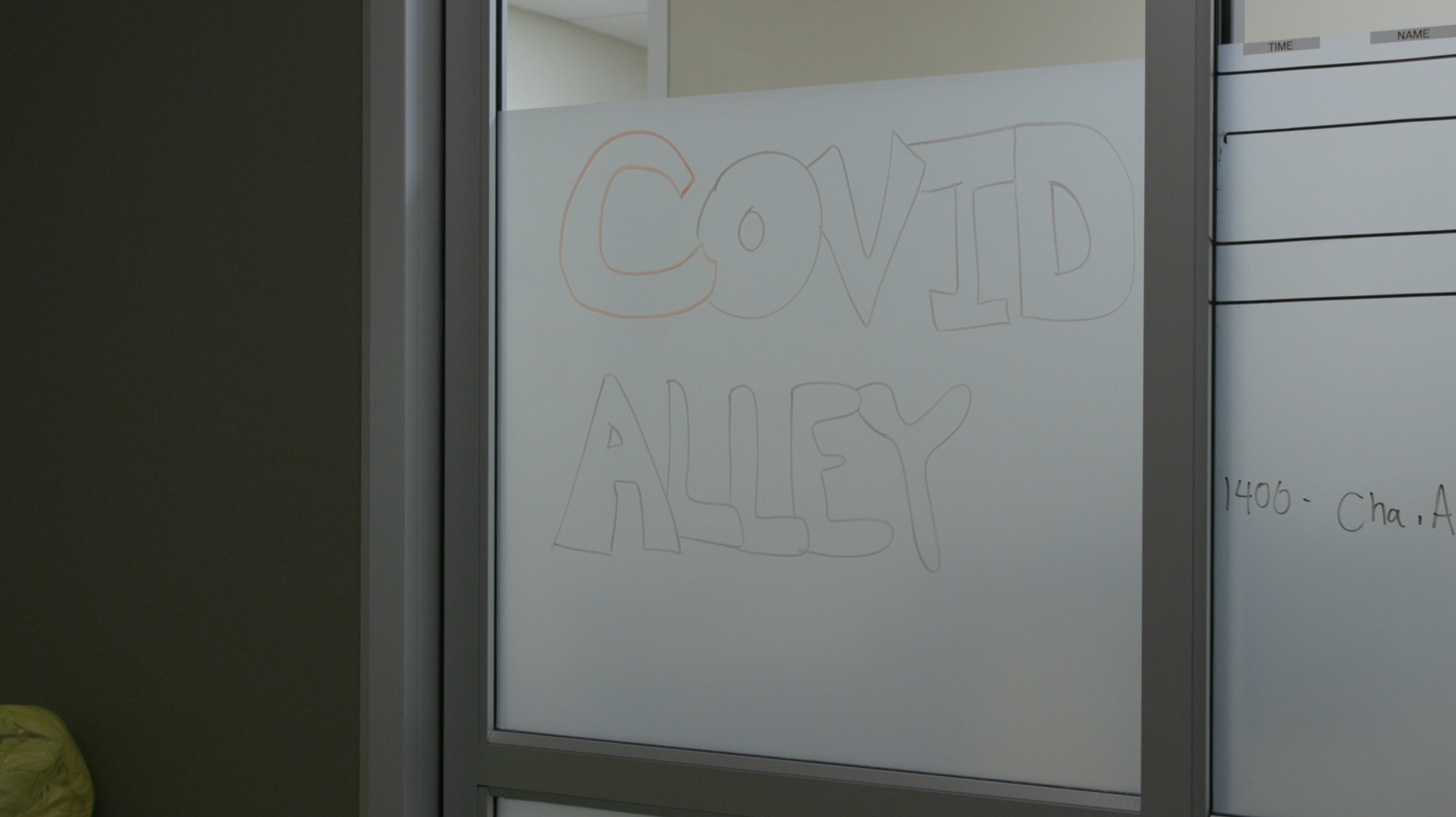 A glass door with "COVID Alley" written in dry erase marker