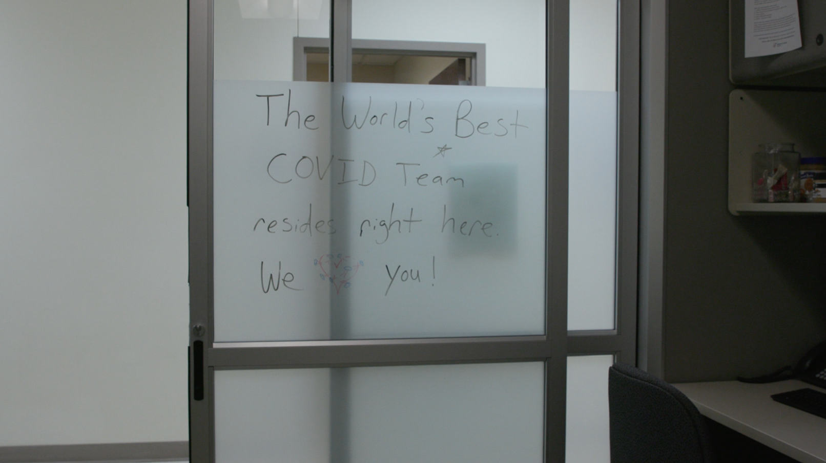 A glass door with a handwritten note reading "The World's Best COVID Team resides right here."