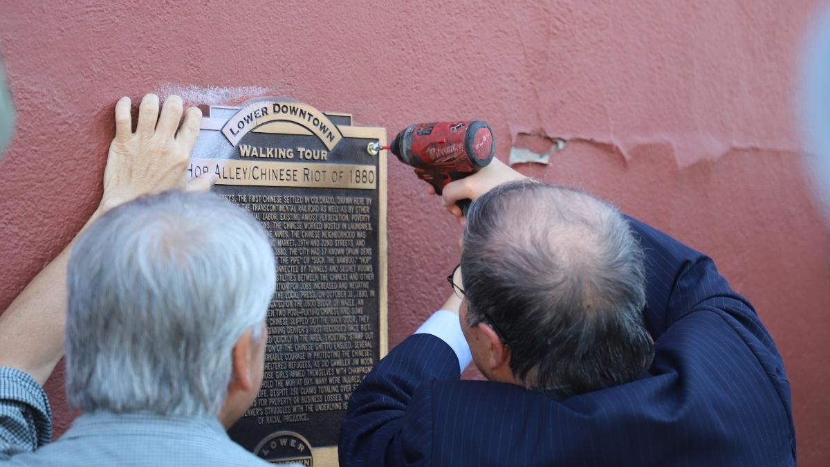 William Wei, right, removes a historical marker in Denver's LoDo neighborhood that inaccurately and offensively described the 1880 anti-Chinese riot in the city.