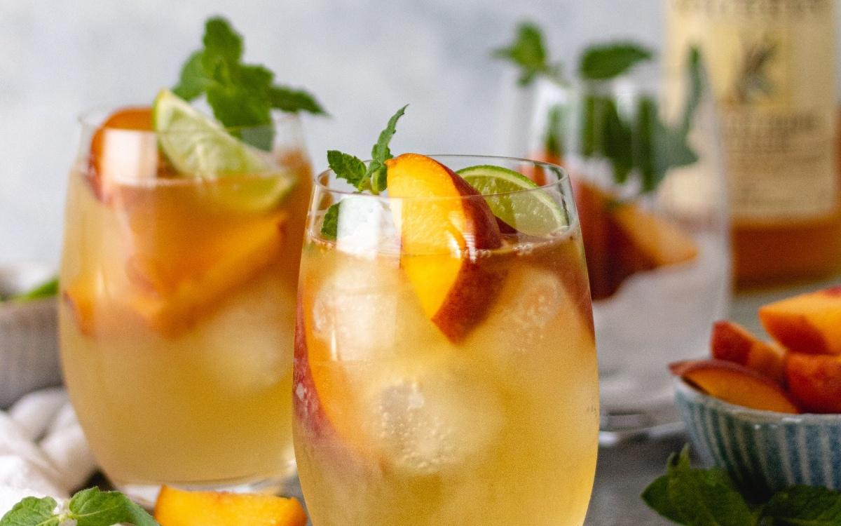 PEach colorad cocktail in a clear rounded wine glass with ice