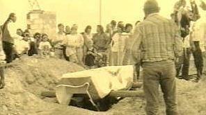 Image of the casket of Zintkala Nuni, the Lost Bird being lowered into the ground. Many people are standing near the grave. 