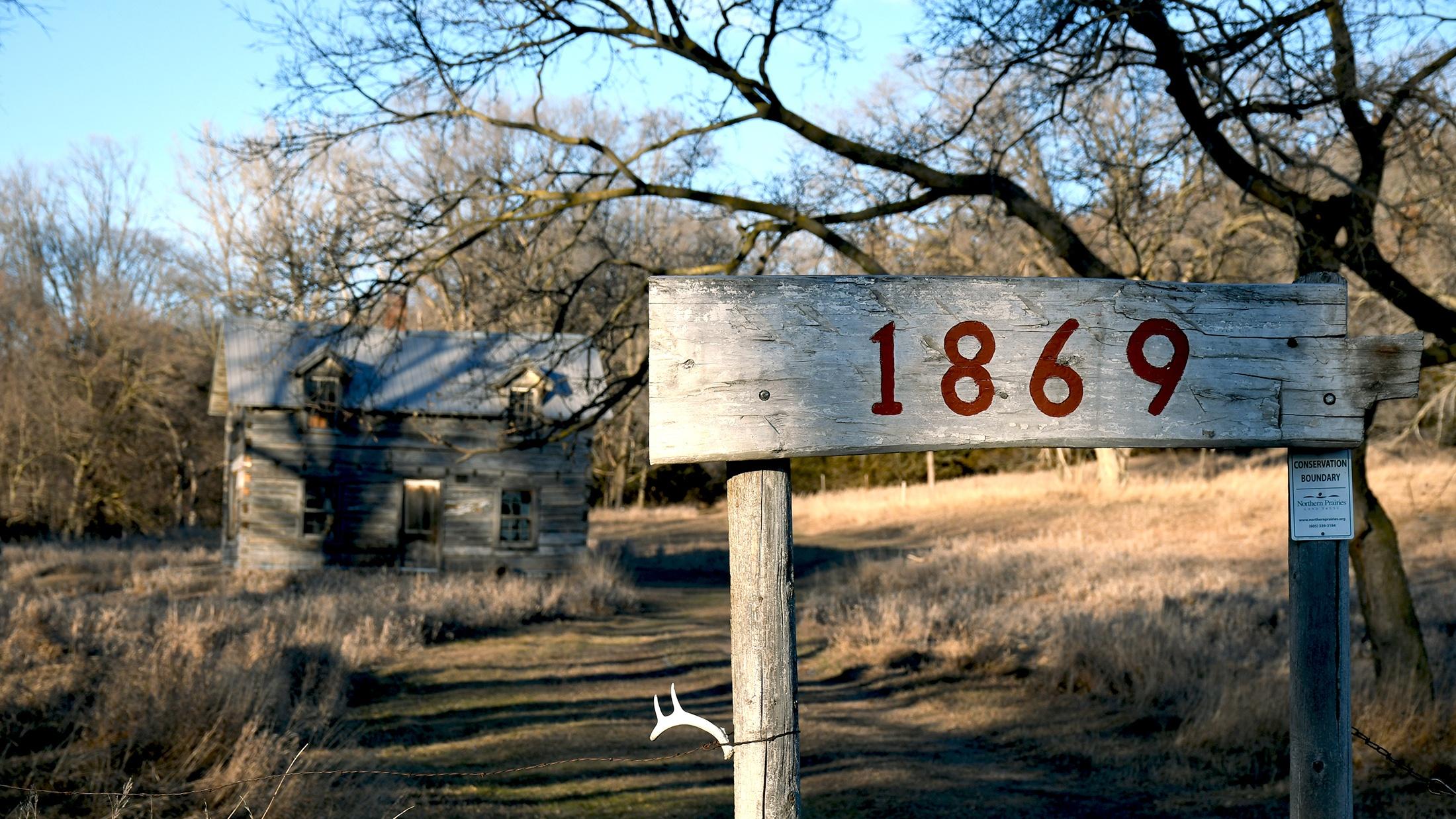 Photo of a log home with an 1869 sign in front of it. 