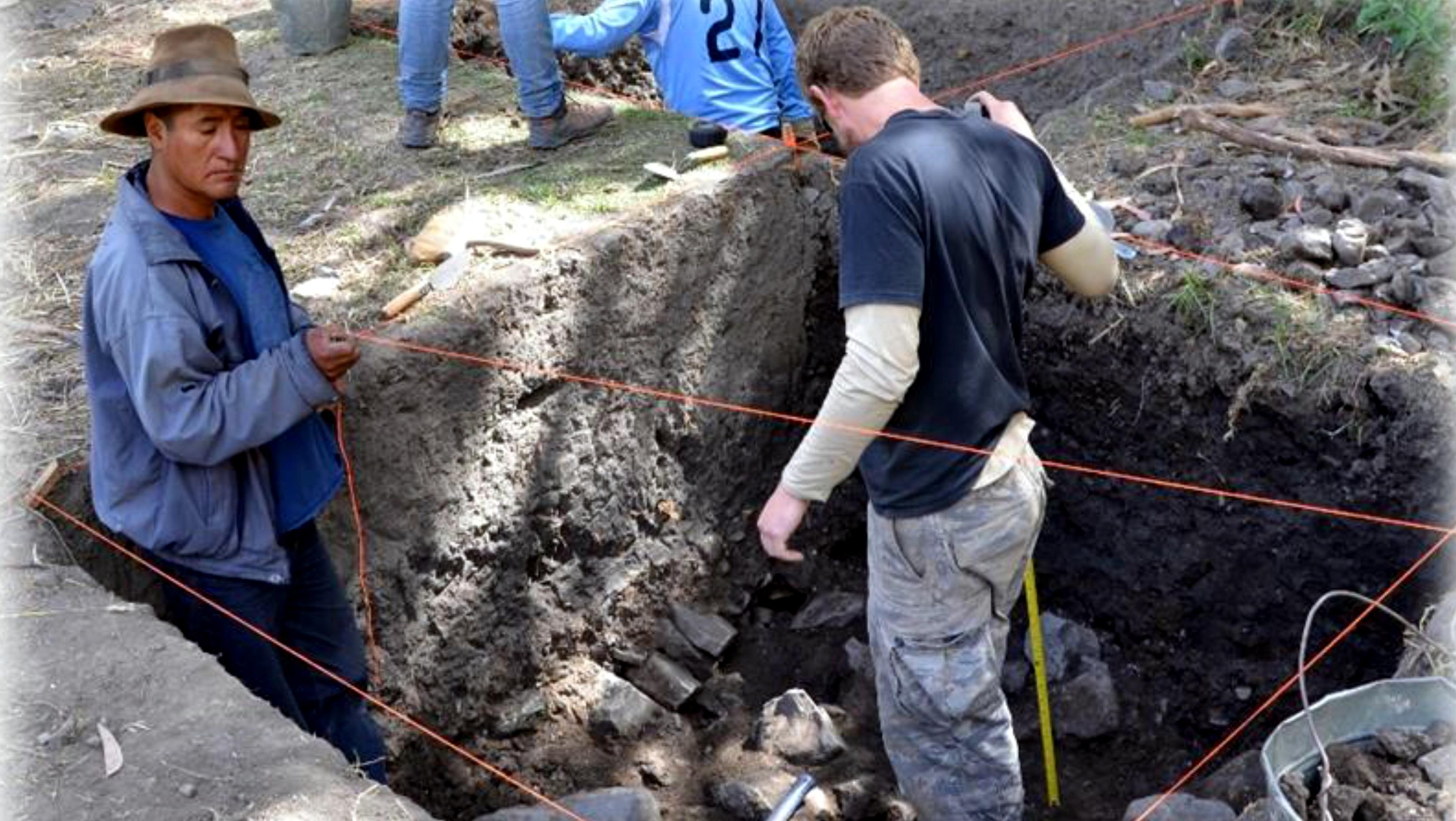 Archeological dig with two men inside of a cubical shaped hole. 
