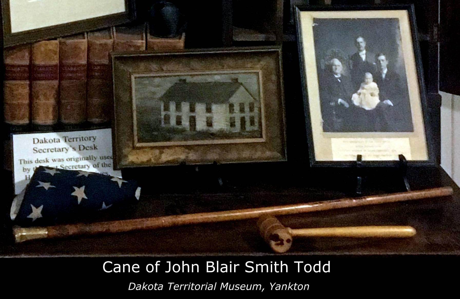 An old wooden desk with a cane, a U.S. flag, and two pictures sitting on it. 