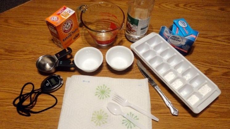 Image of items used in the activity, including a stopwatch, measuring cup, two small bowls, baking soda, ice cube tray, vinegar, and effervescent tablets.