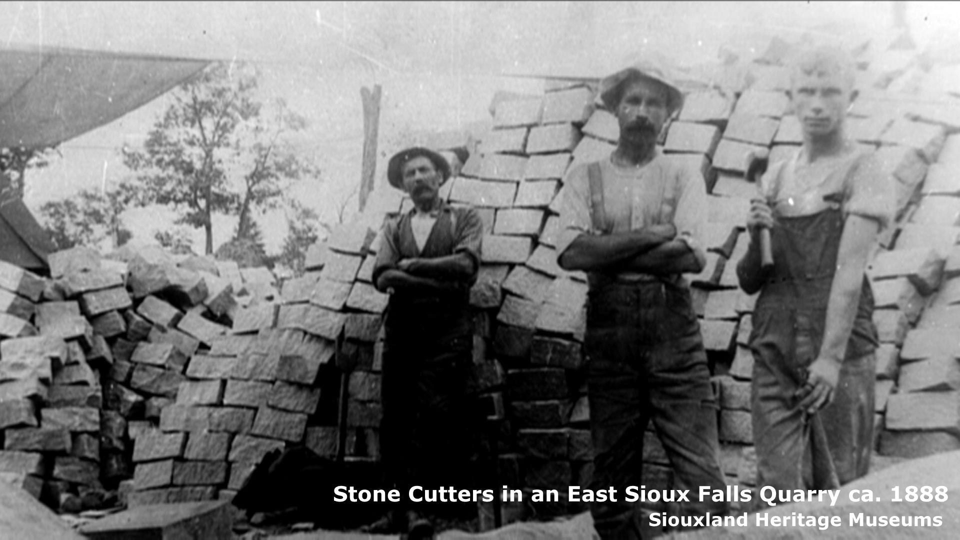 This is an archival photo of three stone cutters standing in front of many large blocks of quartzite. 