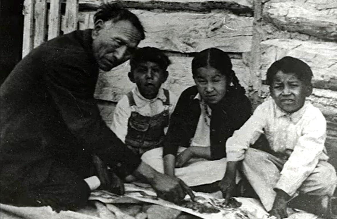 Archival photo of an older Native American man with three Native American children. 