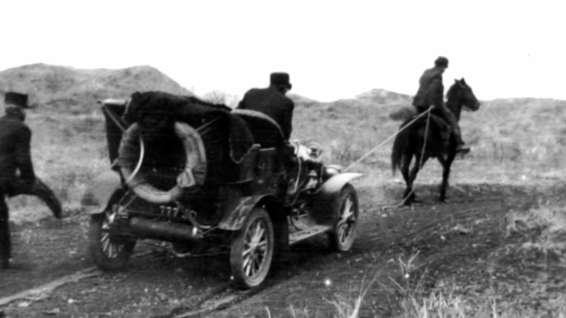 Archival image of a horse and rider pulling out an Model T Ford stuck in mud. 