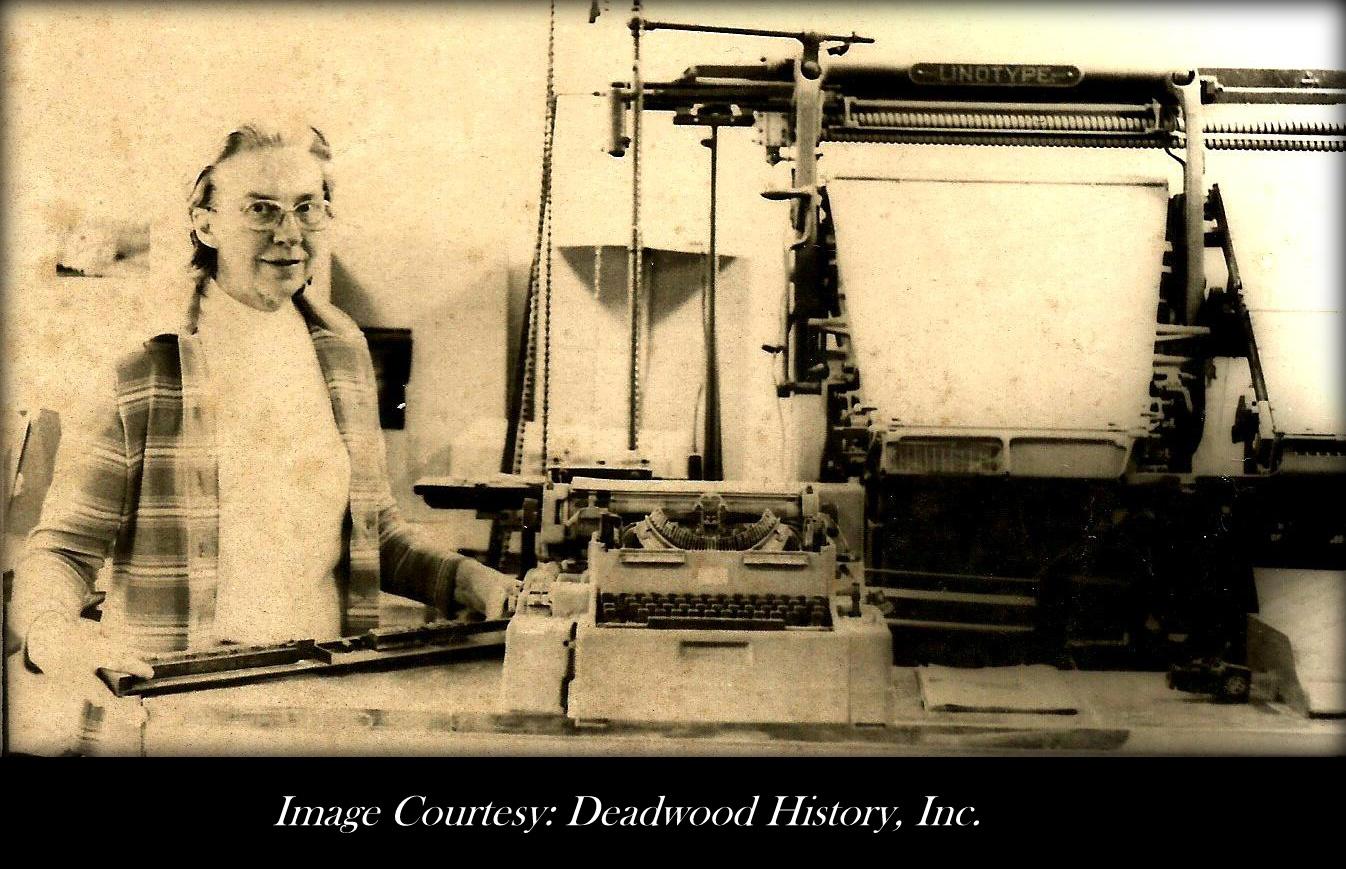 An archival photo of a woman standing next to a printing press. 