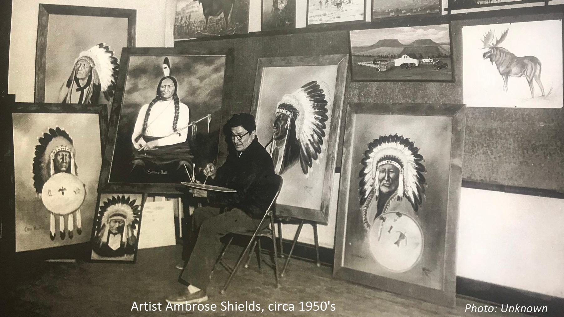 Photo of artist Ambrose Shields sitting in front of his paintings. 