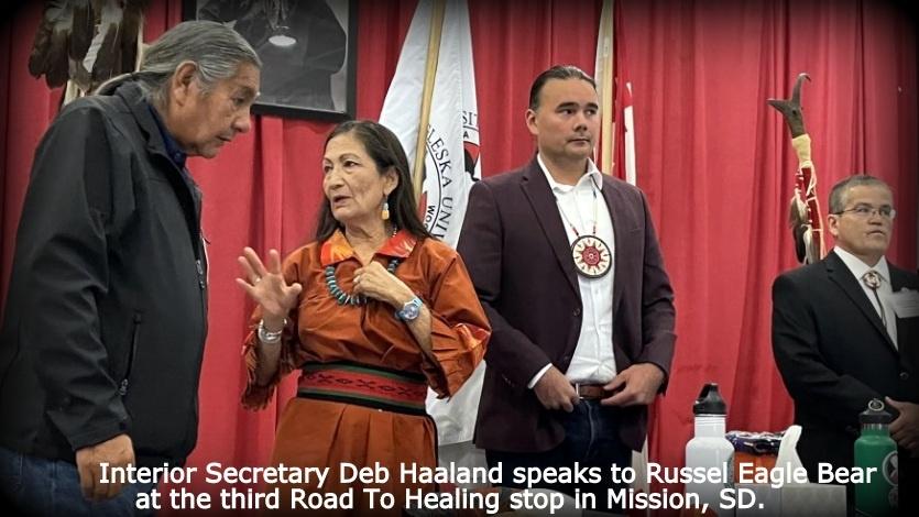 Photo of Interior Secretary Deb Haaland speaking to Russel Eagle Bear, two other men are standing in the background. 