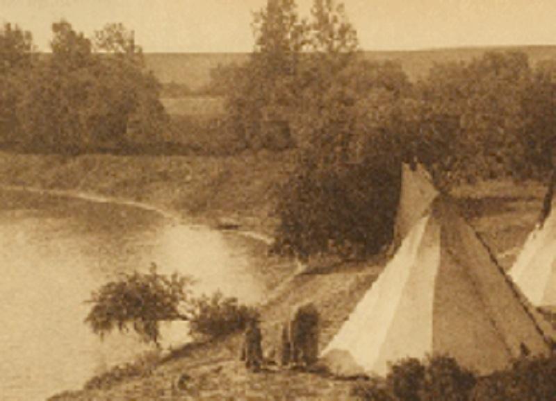 Archival photo of a teepee next to a pond with trees in the background. 
