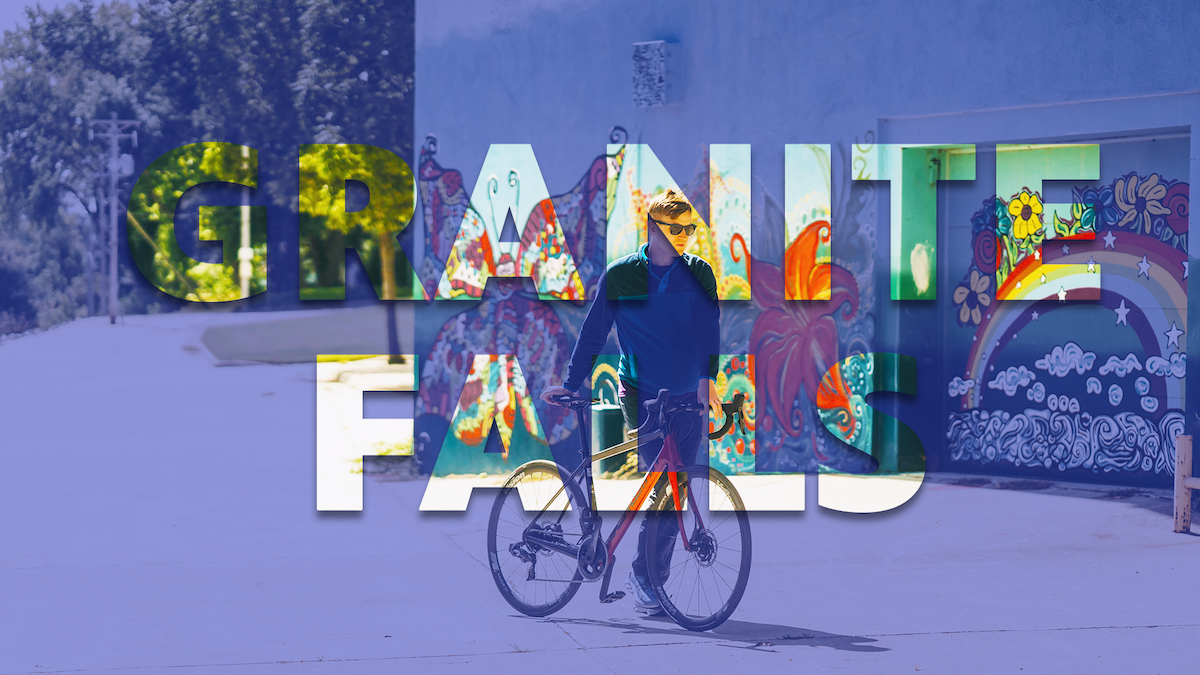 A photo of Mikah Meyer walking his bike in front of mural in Granite Falls.