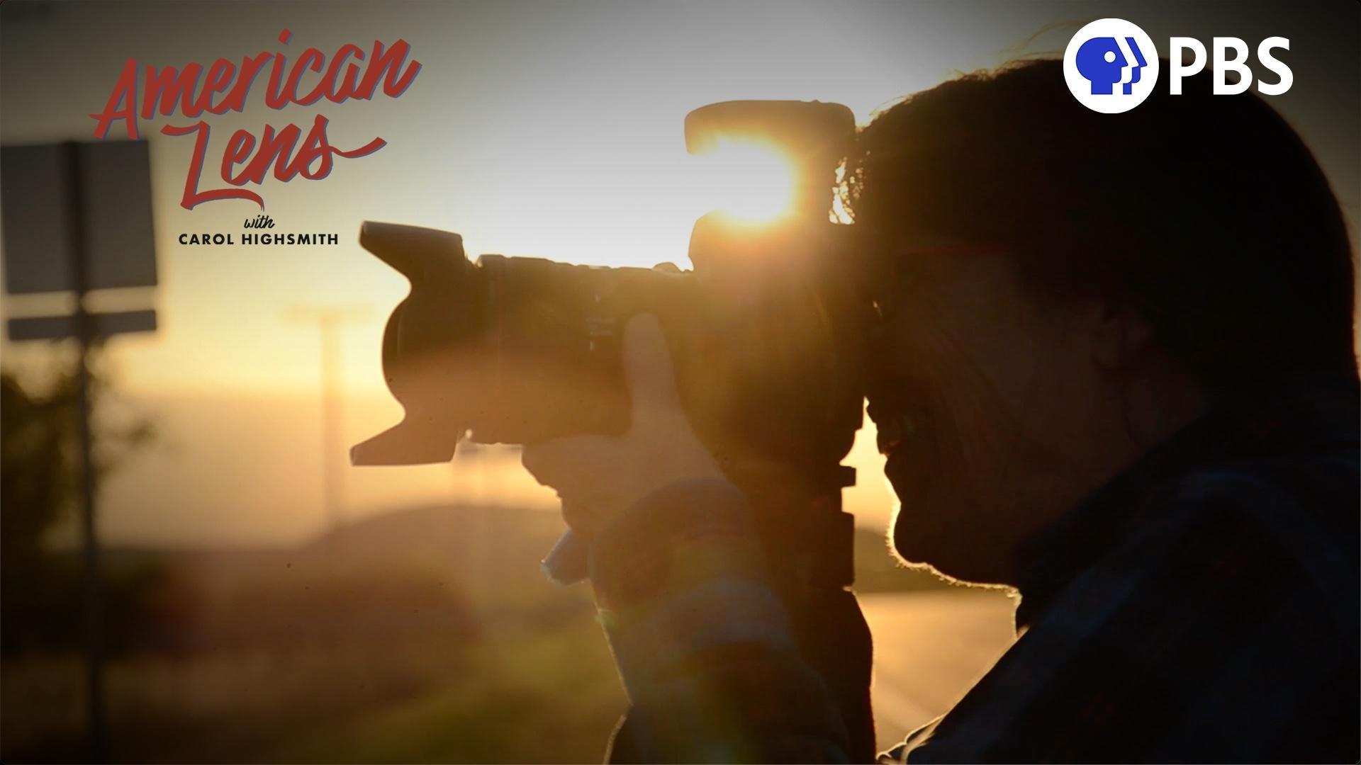 During a sunrise photographer Carol Highsmith is photographed in shadow silhouette as she hold a camera to her eye to take a photograph. The title of the program is American Lens with Carol Highsmith.