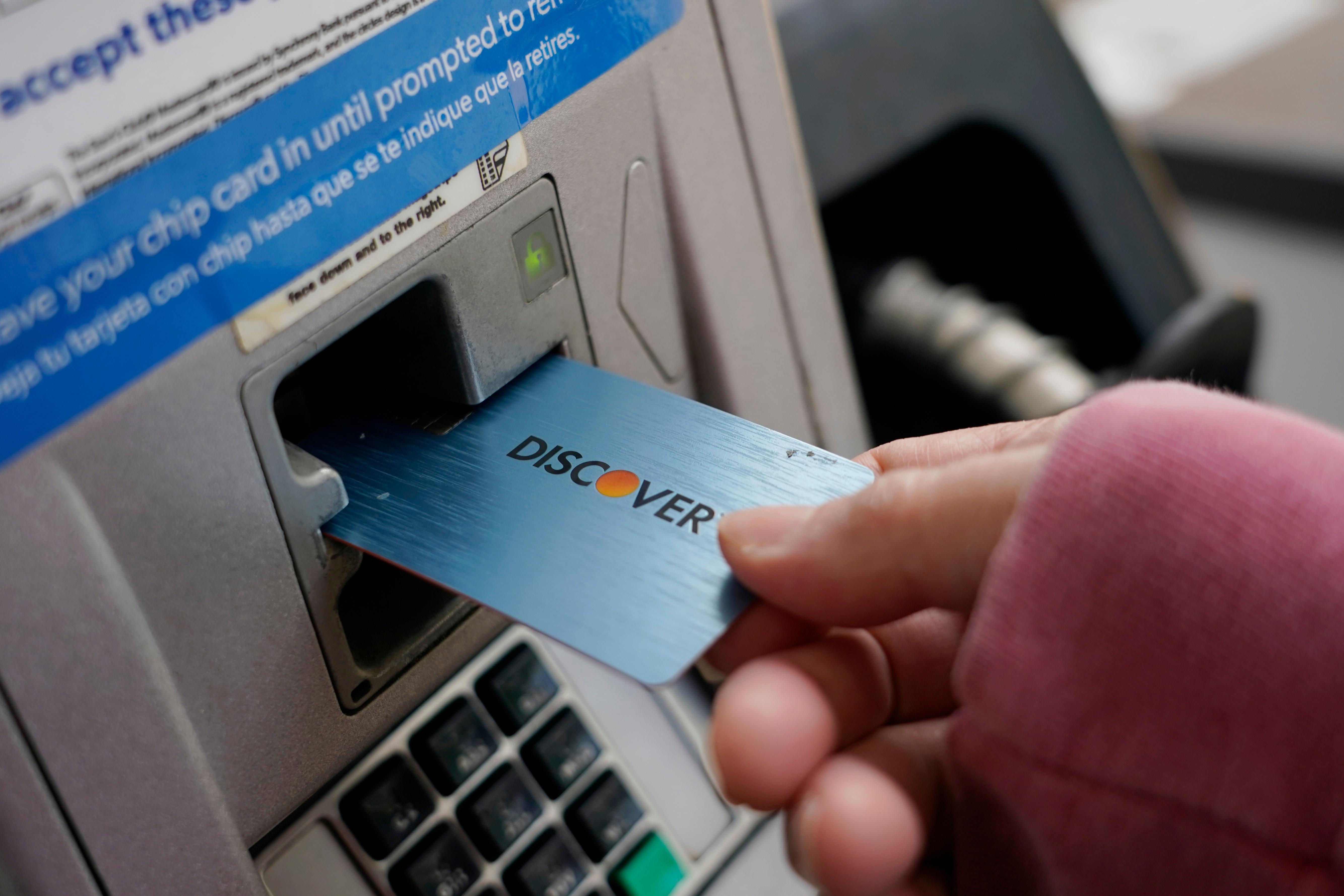 A person holds their credit card up to a gasoline kiosk.