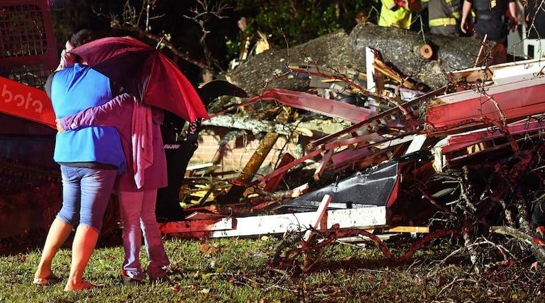 Two people hug under an umbrella as they look at first responders freeing a victim from a house.