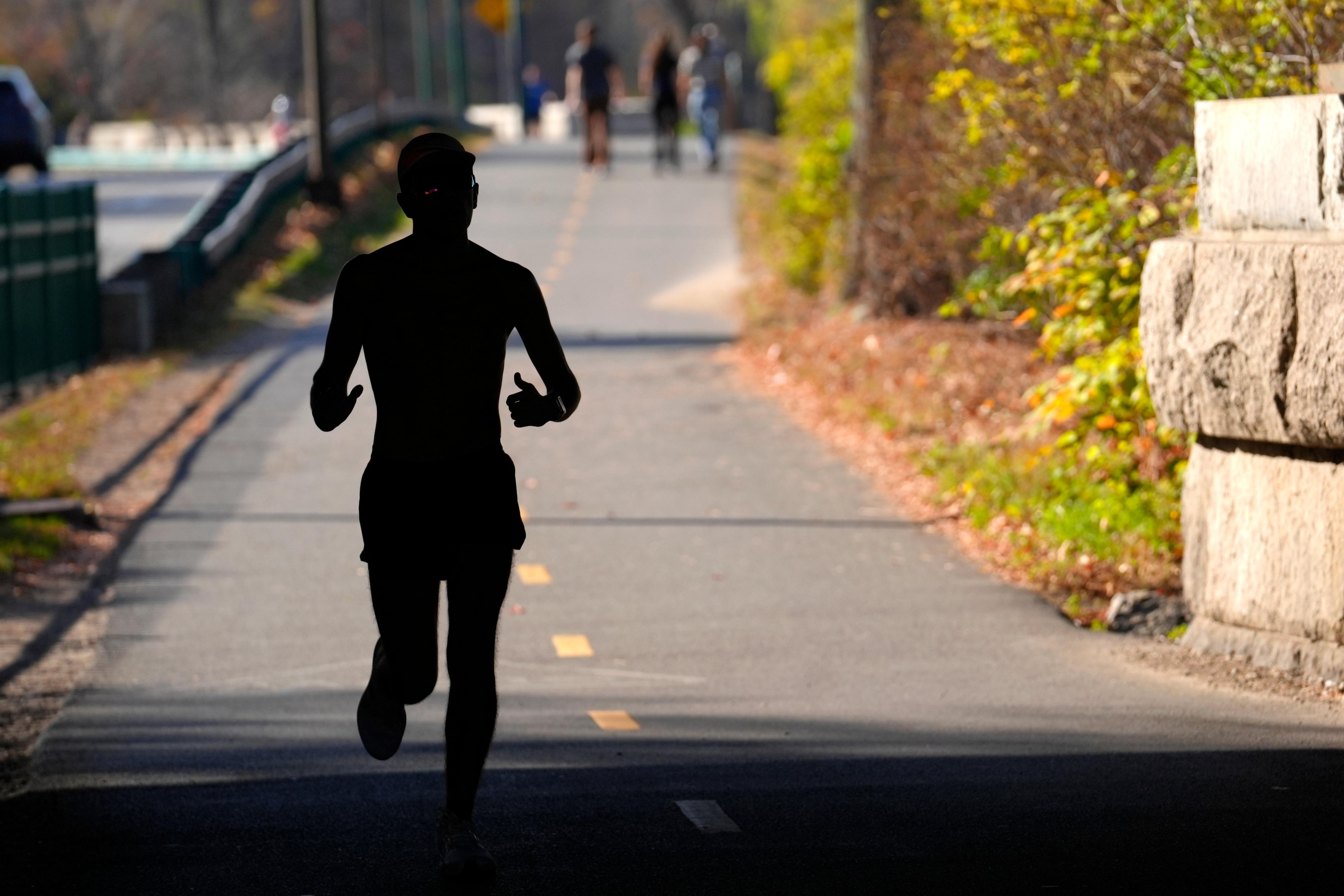 A runner appears in silhouette while running in temperatures in the 70s, Wednesday, Nov. 6, 2024, under a bridge near the Charles River, in Boston.