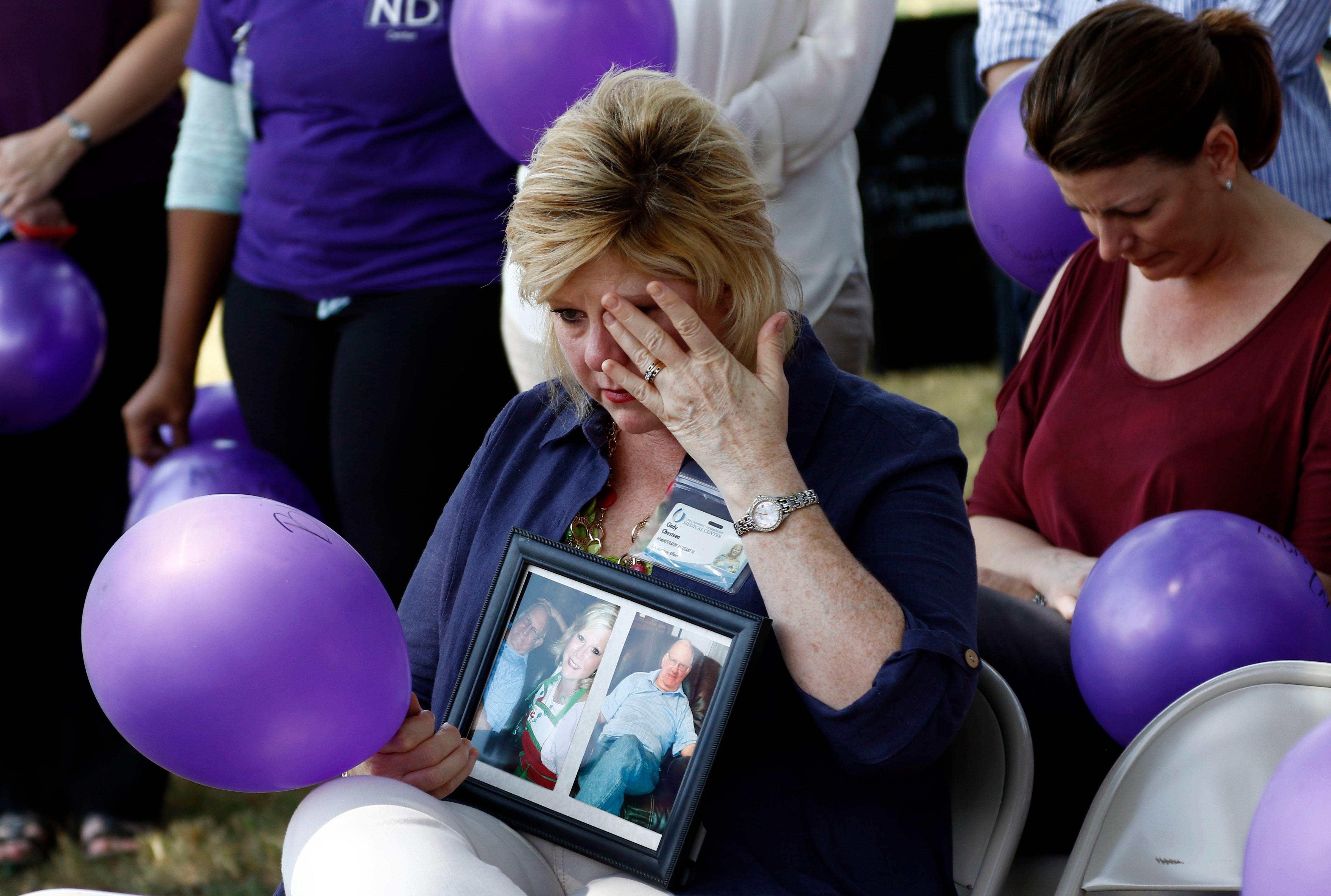 A woman holds a photograph of her father as she wipes away tears.